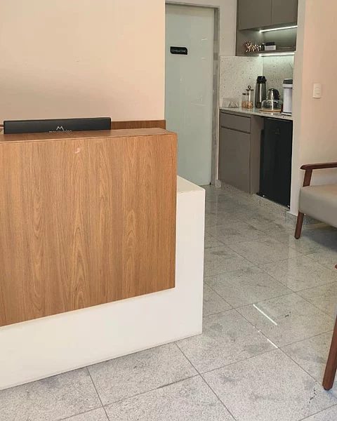 A recepção, com o balcão de madeira, a porta do consultório e a área de café ao fundo