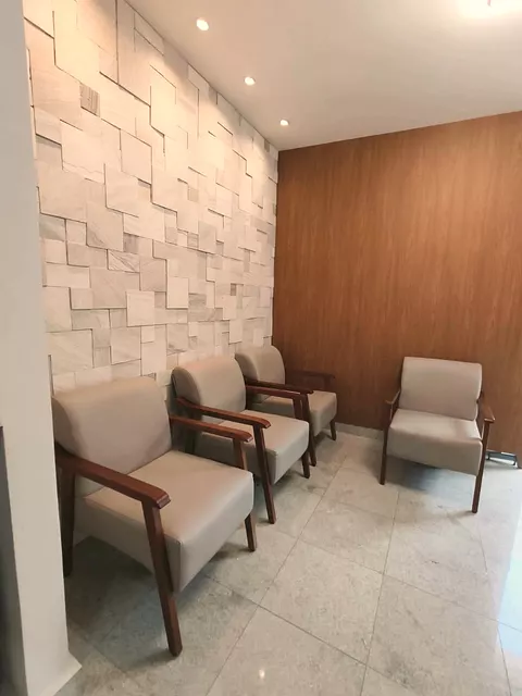 A sala de espera, com quatro poltronas, a parede de pedra clara e o painel de madeira